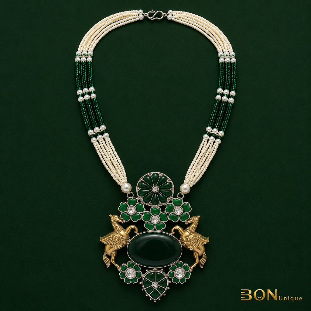 Full view of antique gold dual Pegasus necklace with multi-strand green bead and pearl chain on dark green background