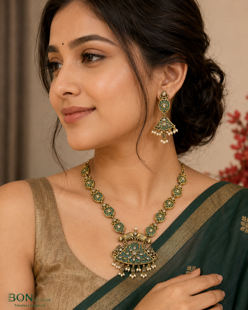 Model wearing antique gold dual elephant necklace set with teal enamel and pearl drops on green saree