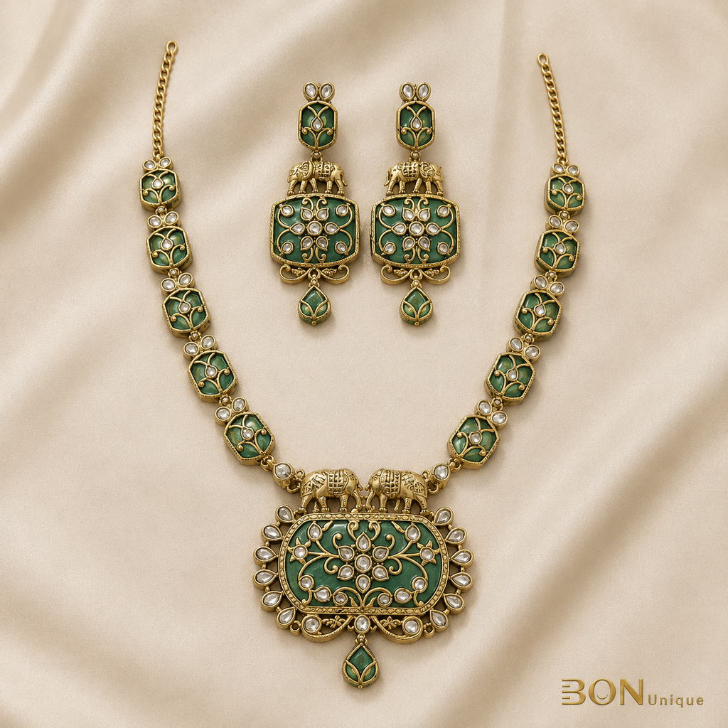 Full set view of antique gold elephant necklace with green enamel chain links and matching elephant earrings on cream fabric