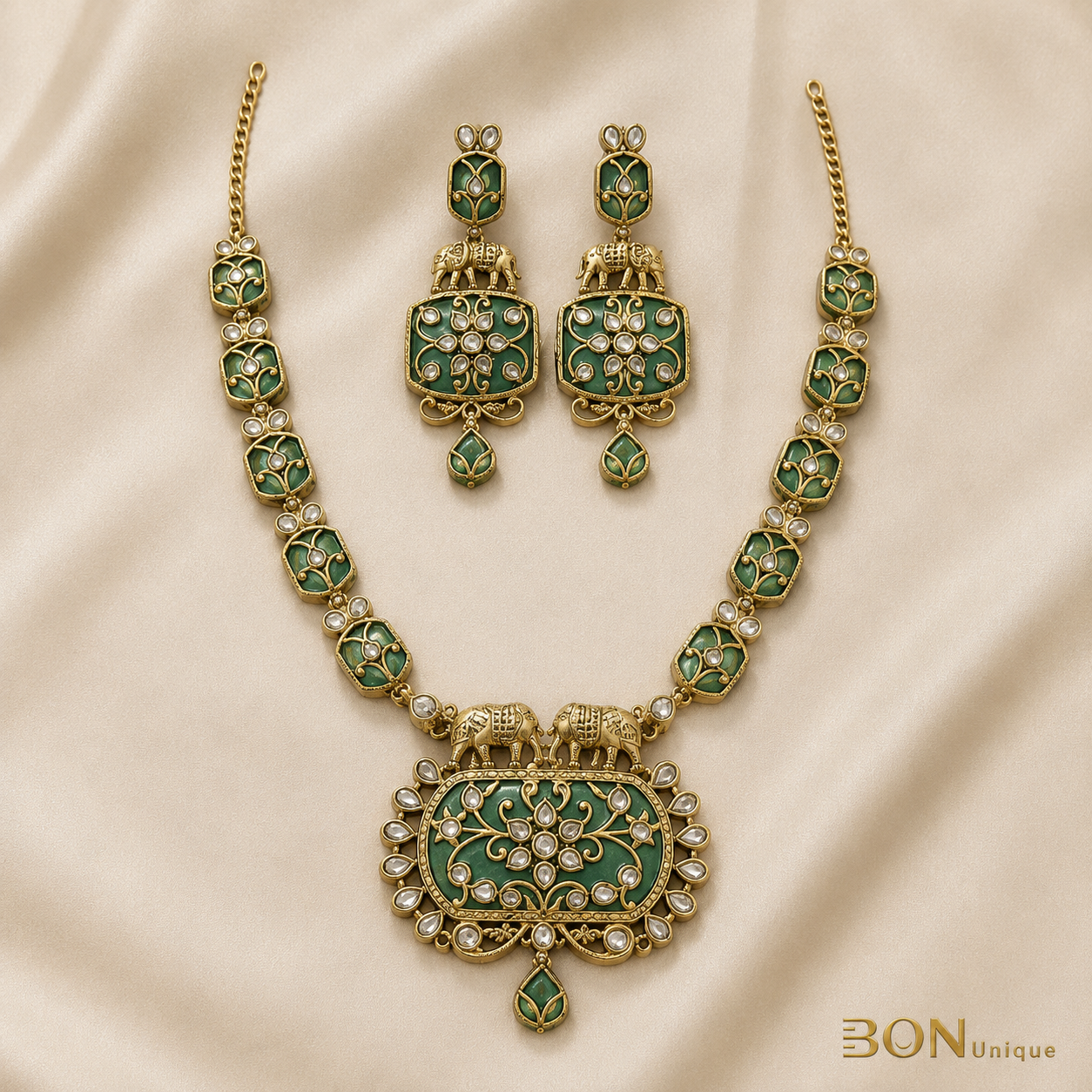 Full set view of antique gold elephant necklace with green enamel chain links and matching elephant earrings on cream fabric