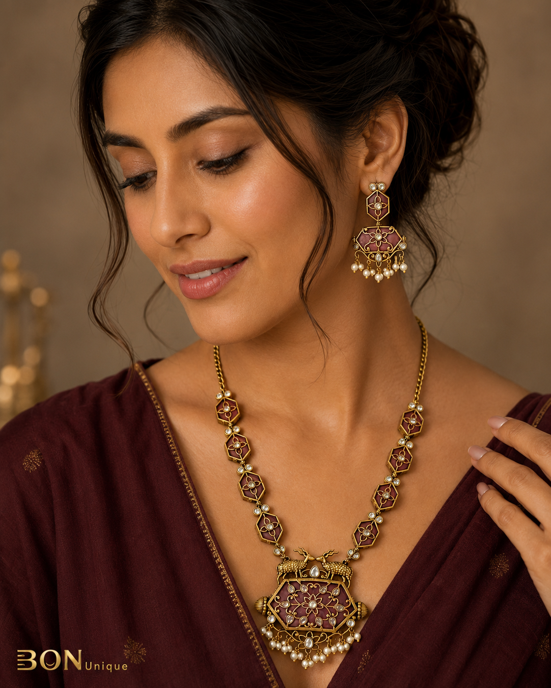 Model wearing antique gold dual deer necklace set with mauve enamel and pearl drops on maroon saree