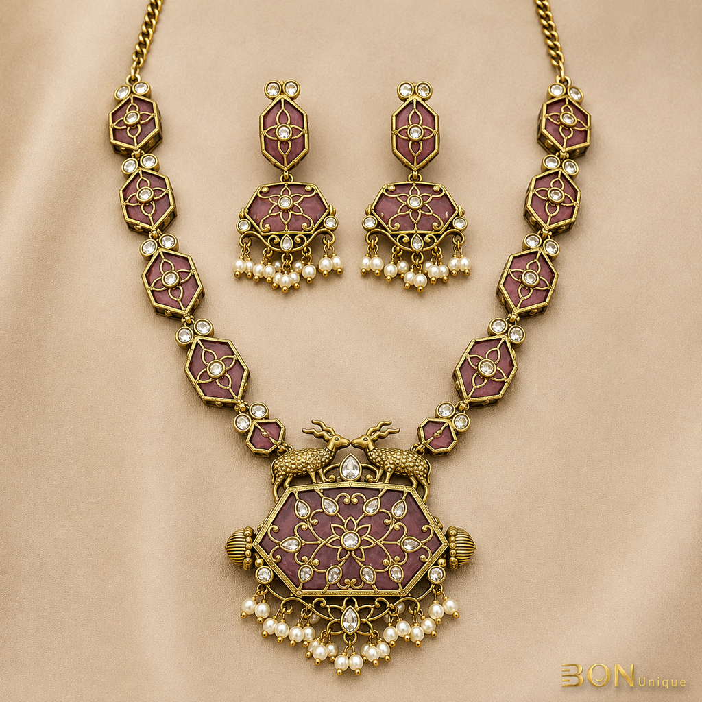 Full set view of antique gold dual deer necklace with mauve enamel hexagonal chain links and matching jhumka earrings on gold fabric