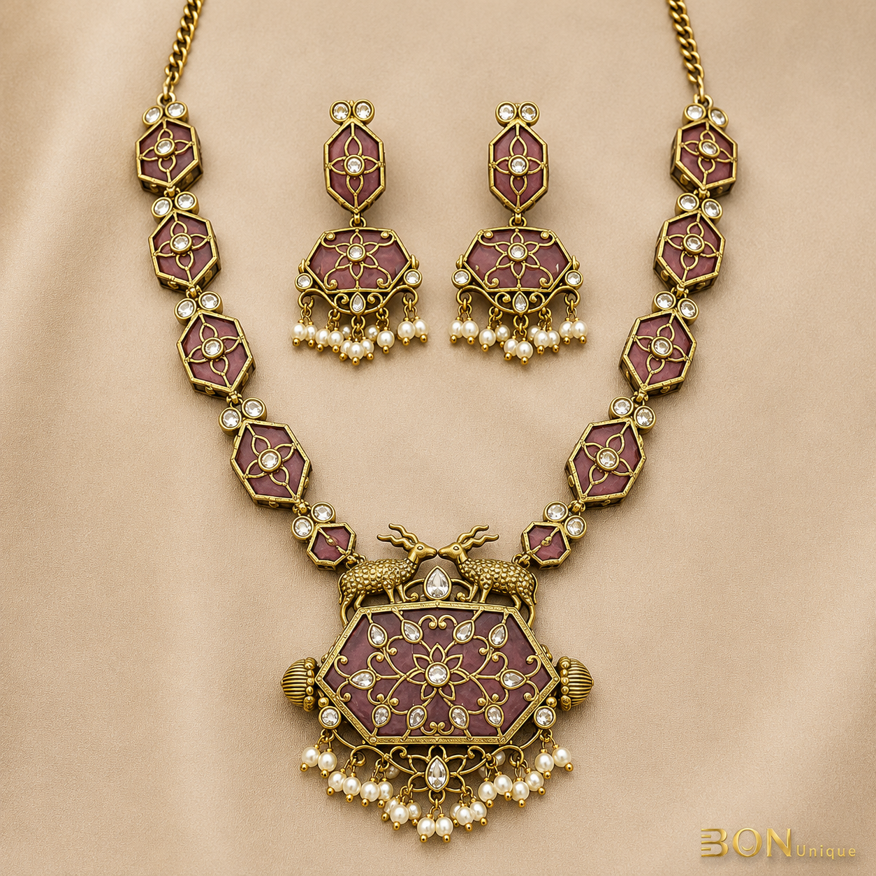 Full set view of antique gold dual deer necklace with mauve enamel hexagonal chain links and matching jhumka earrings on gold fabric